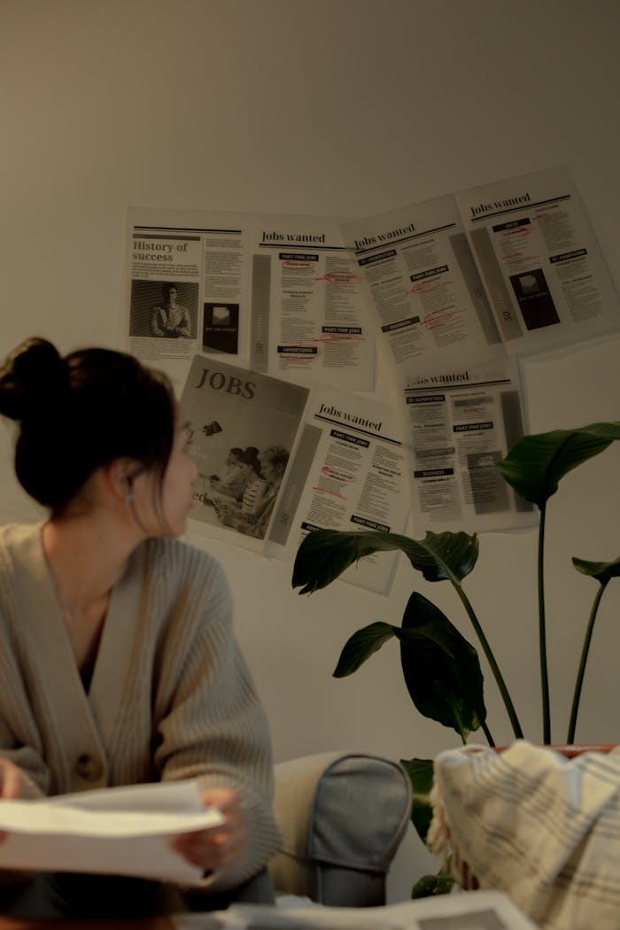 A woman in a cozy setting reviews job listings on a wall, exuding a thoughtful mood.